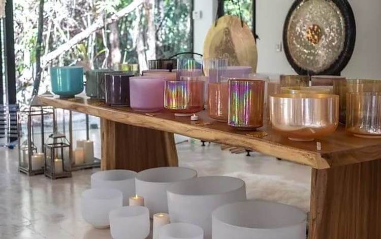 Various candles and singing bowls arranged on a wooden shelf and floor in a bright room with windows overlooking greenery Various candles and singing bowls arranged on a wooden shelf and floor in a bright room with windows overlooking greenery