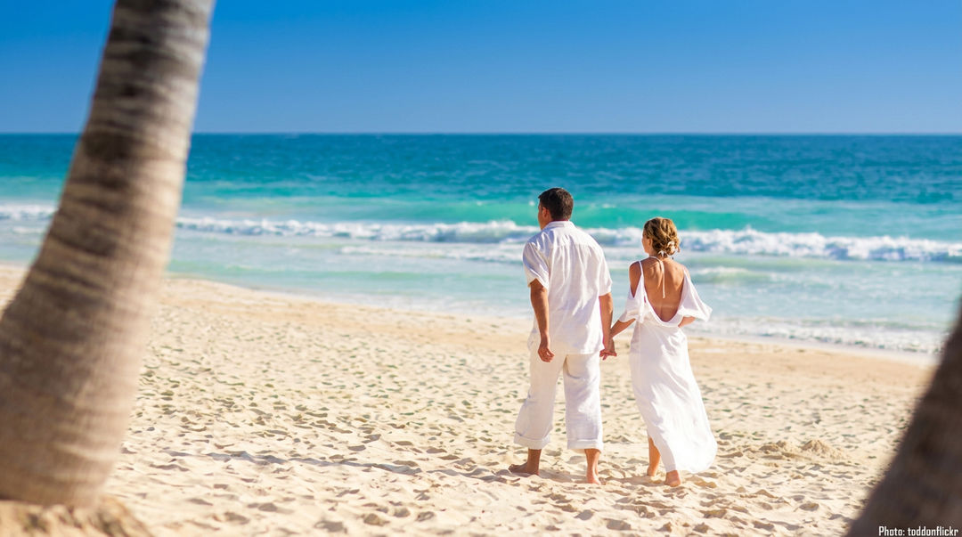 Organizadores de bodas venden cenotes en lugar de playas Pareja vestida de blanco camina de la mano por la playa, con el mar y las olas de fondo