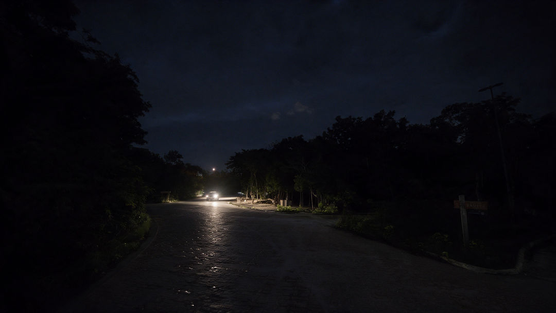 Why Tulum’s streets are going dark A dimly lit street lined with trees shows sparse streetlights illuminating a mostly dark roadway at night