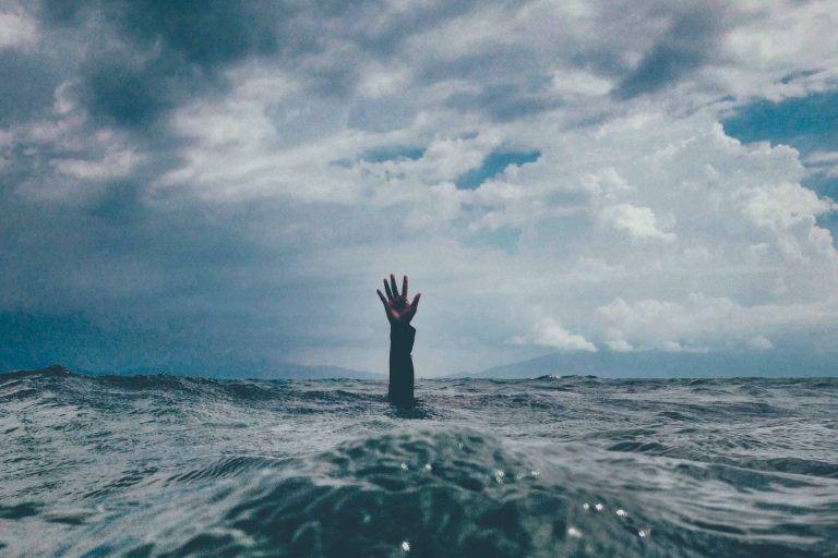 A hand reaching out from the water in the middle of the ocean.