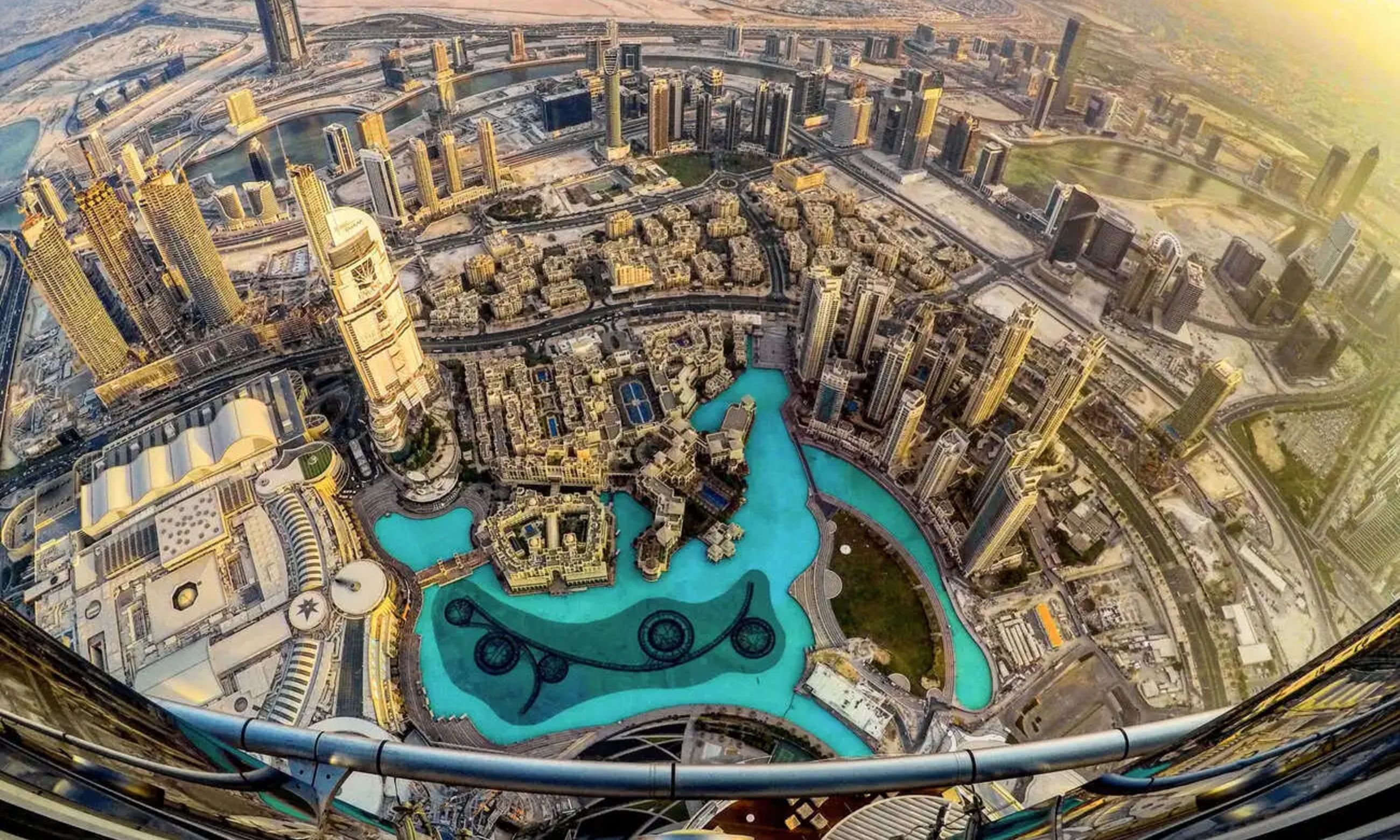 Aerial shot of Burj Khalifa towering above Downtown Dubai, with the Dubai Fountain and The Dubai Mall visible below.