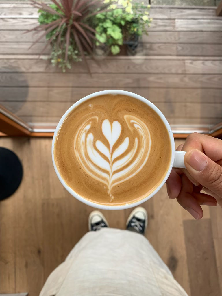 aerial shot of a cafe late in a cup held by yumi with a beautiful late art applied