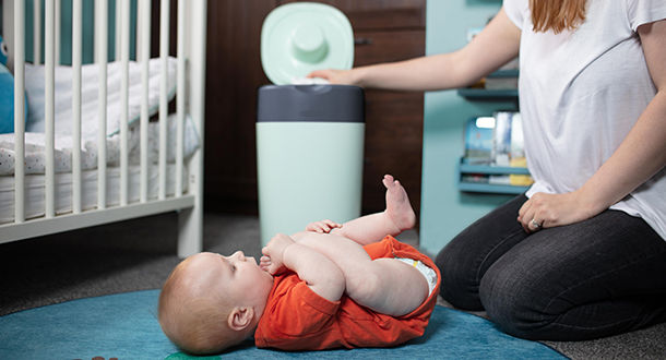 Mother putting nappy into nappy disposal bin with baby lay on floor