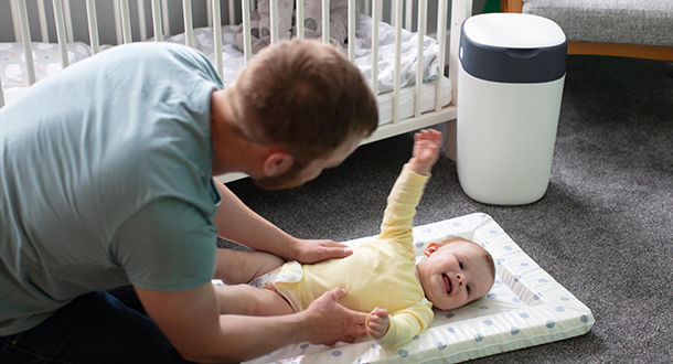 Father holding baby on the floor with nappy disposal bin in the back ground