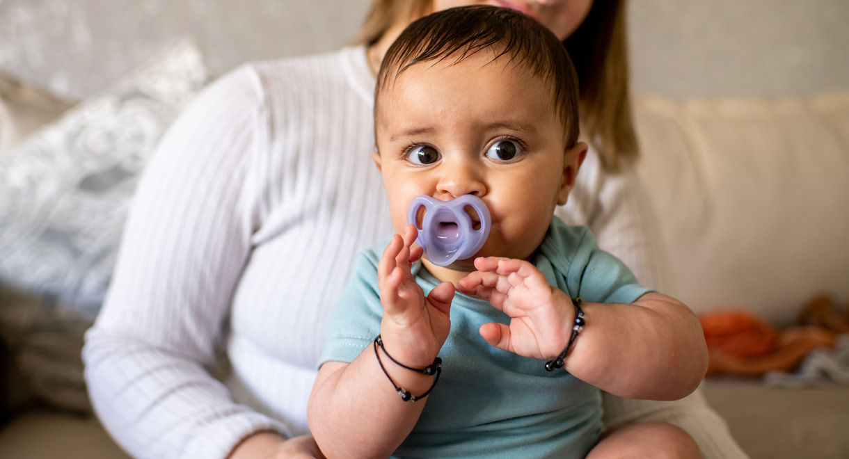 Child sucking on ultra light soother whilst sat on mothers knee 