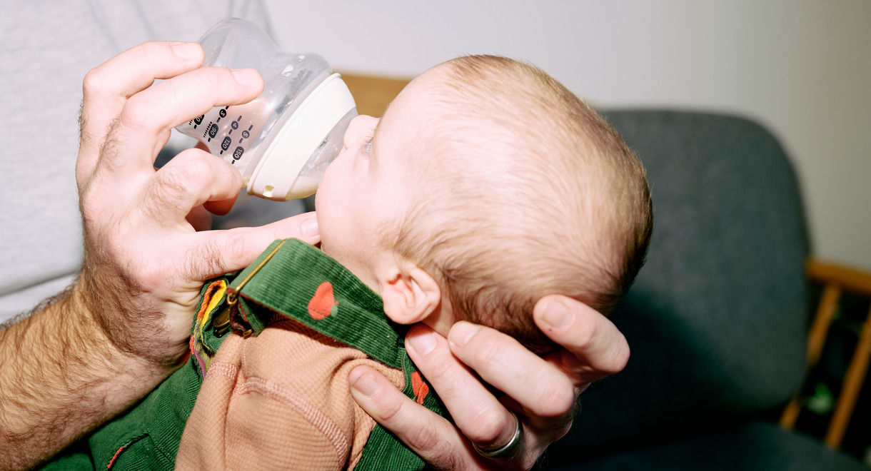 Padre sosteniendo al bebé y alimentando leche de botella de inicio natural