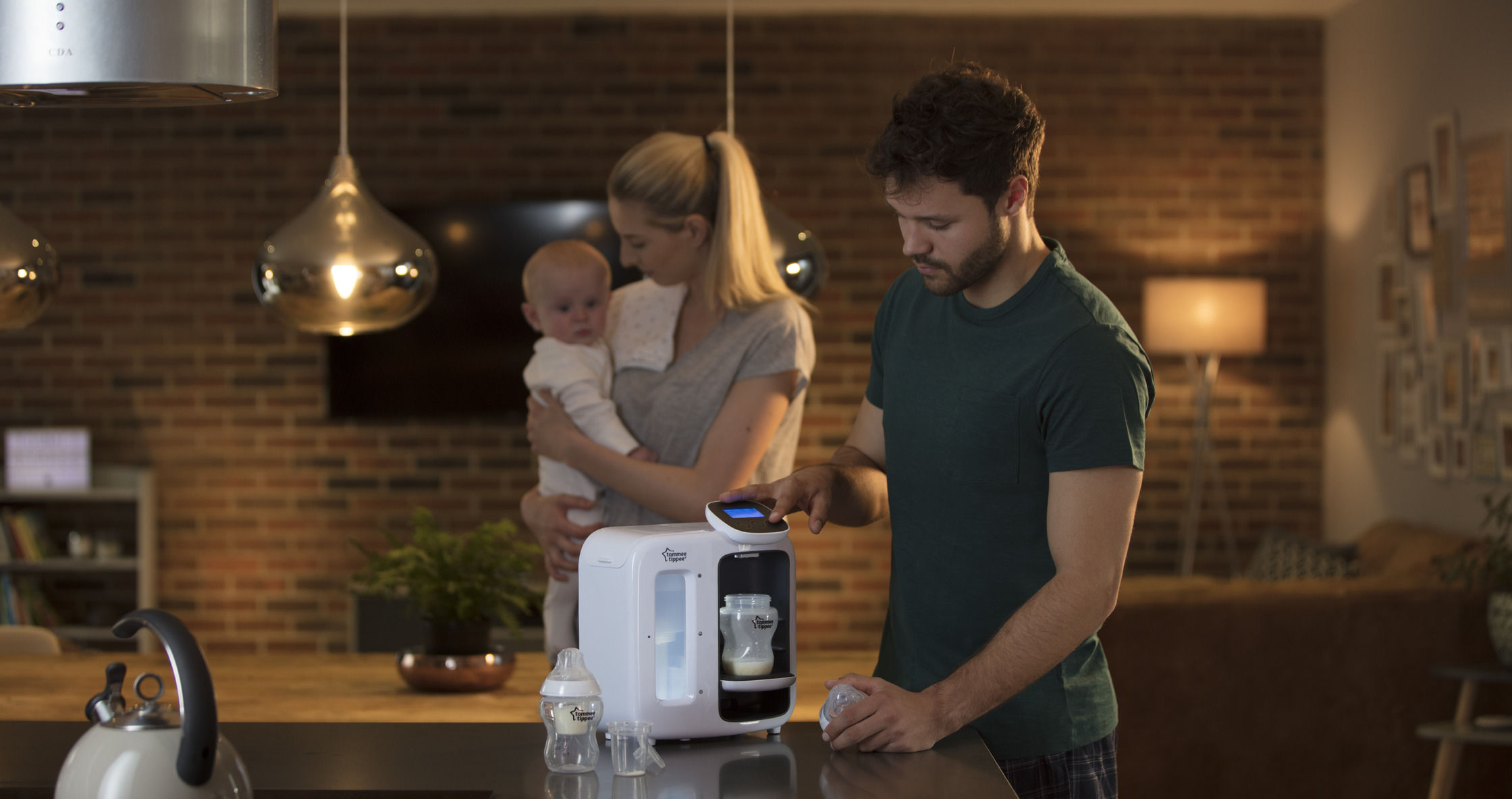 Padre usando Perfect Prep Day & Night en una cocina con su madre cargando a su bebé al fondo