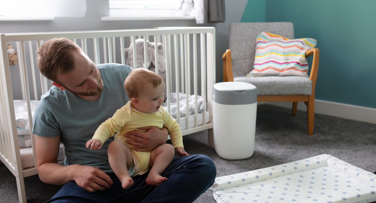 Father holding baby on his lap in bedroom with nappy bin in the back ground