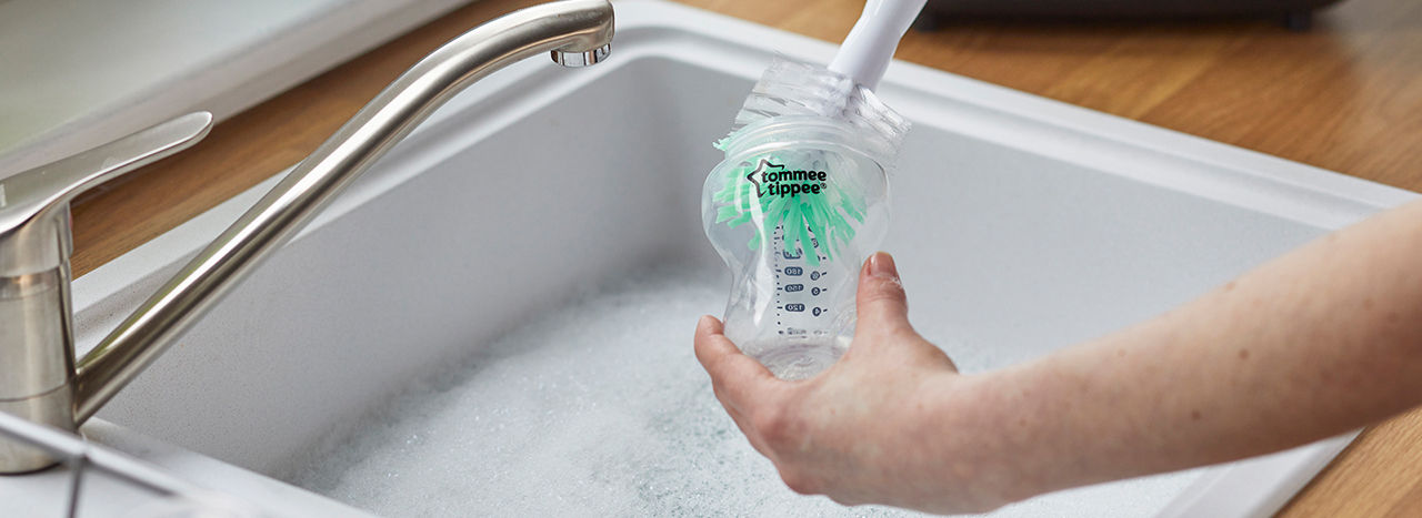 Quelqu'un nettoyant à l'intérieur d'une bouteille au-dessus de l'évier de la cuisine avec la brosse de la bouteille