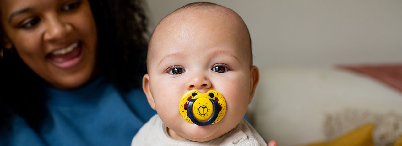 Close up of baby's face with fun style soother in their mouth