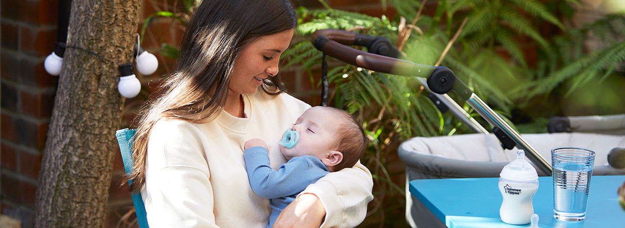 Mother holding baby whilst sat outside, the baby is sucking on an ultra light soother 