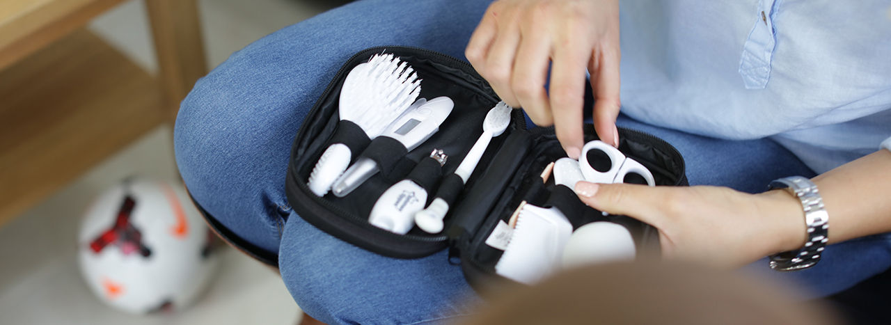 Women holding an open hea,thcare kit showcasing what is included - 1x digital oral thermometer, 1x hairbrush, 1x comb, 1x nail scissors, 1x nail clippers, 1x nasal aspirator, 1x toddler toothbrush and 2x emery boards