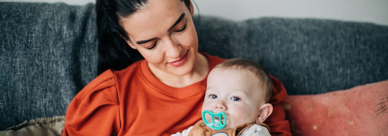 Baby sat on mother lap sucking on soother