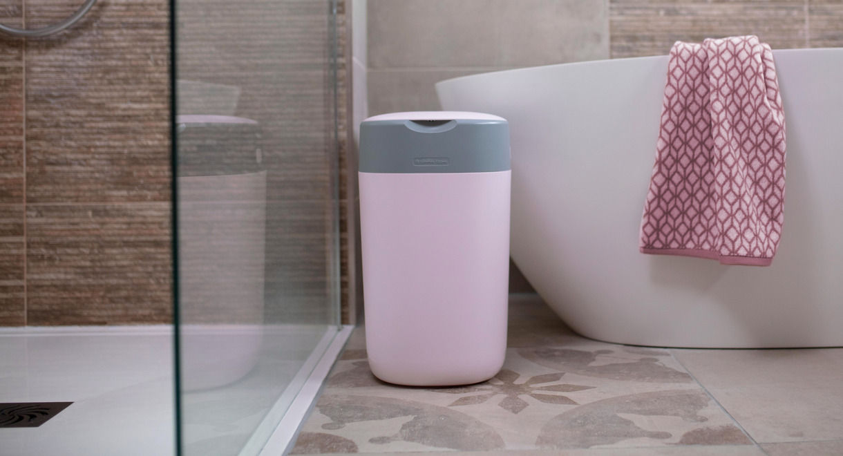 Mother putting nappy into nappy disposal bin with baby lay on floor