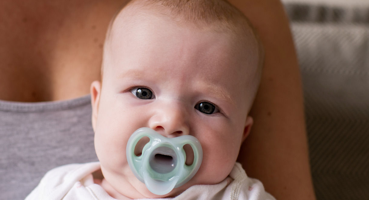 Close up of baby sat on mothers lap with Ultra-light pacifier in their mouth