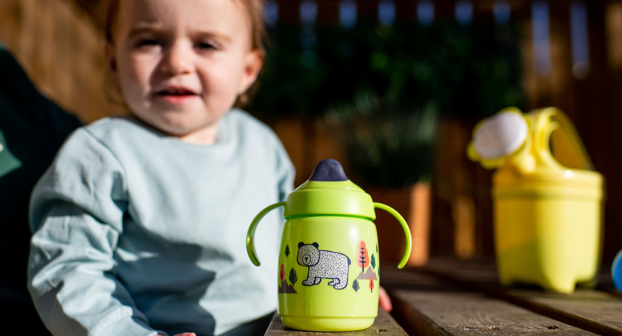 Green trainer sippee cup on park bench with toddler in the background