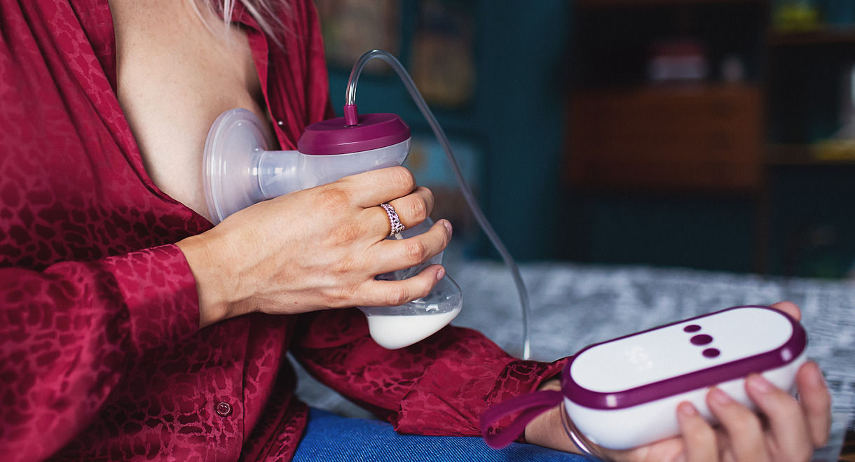 Close up of women using single electric breast pump whilst sat edge of a bed