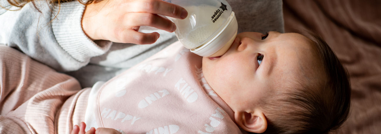 Madre che nutre latte bambino da una bottiglia di PPSU Natural Start mentre il bambino è posato sul ginocchio madre