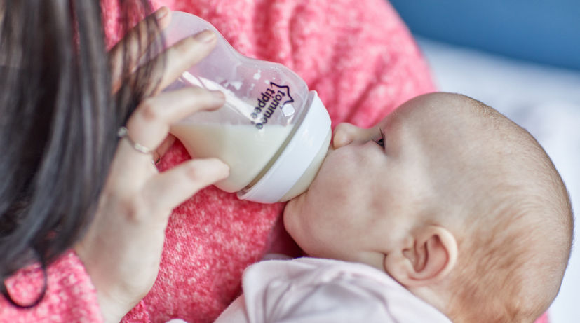 Mother holding baby feeding them milk from a closer to nature bottle