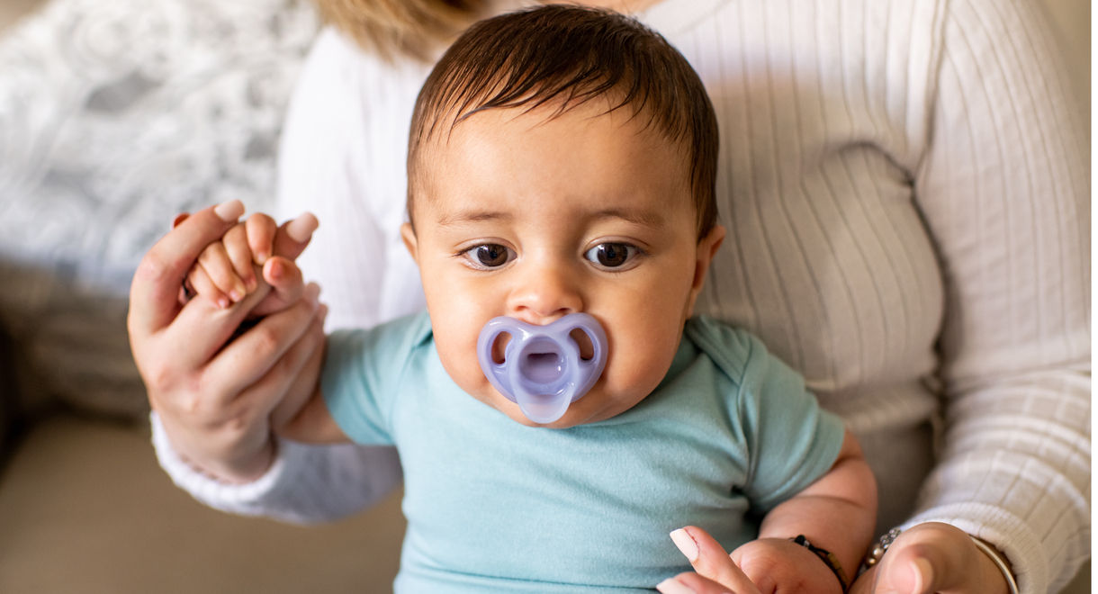 Baby sucking on Ultra-Light Pacifier whilst sat on mothers lap 