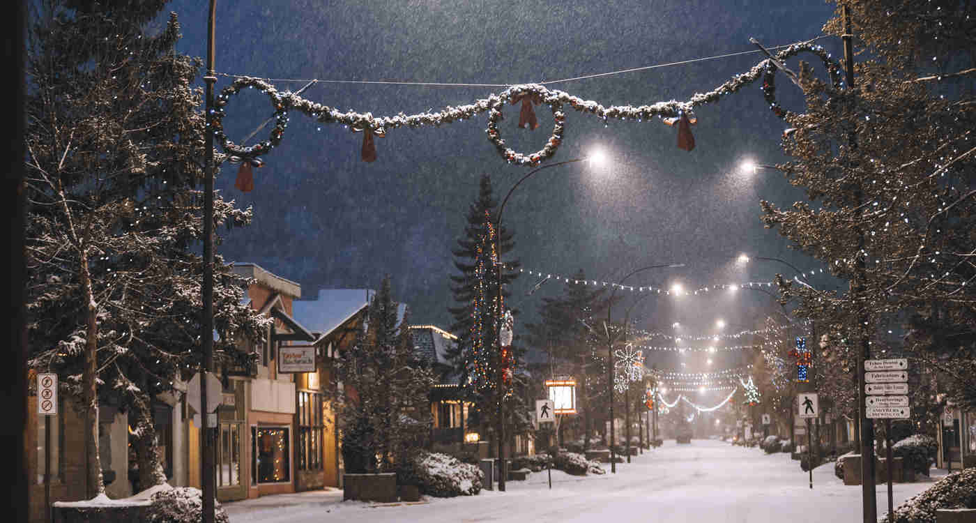 charming small town main street on a snowy night with christmas lights and hanging decorations draped across from side to side and the street covered in snow..