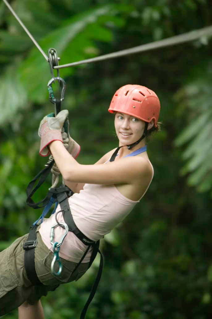 A person smiling while zip-lining through a lush green rainforest.