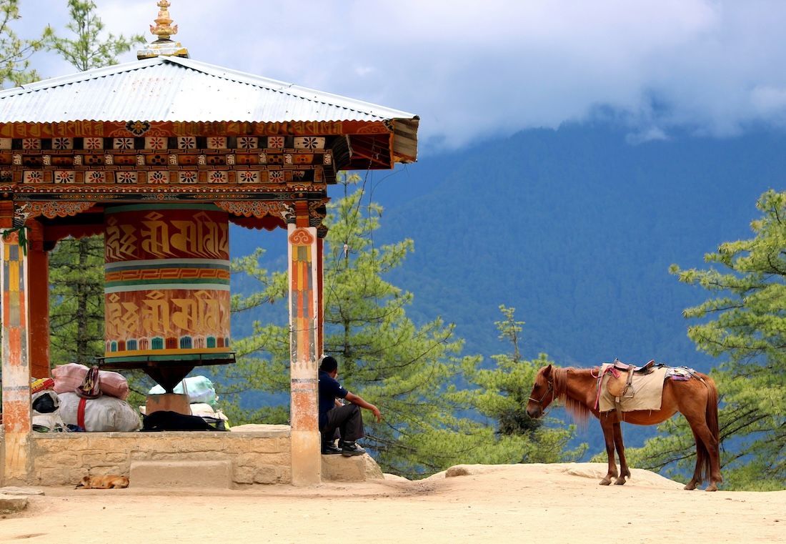 A horse rider takes a break by a prayer wheel in Bhutan