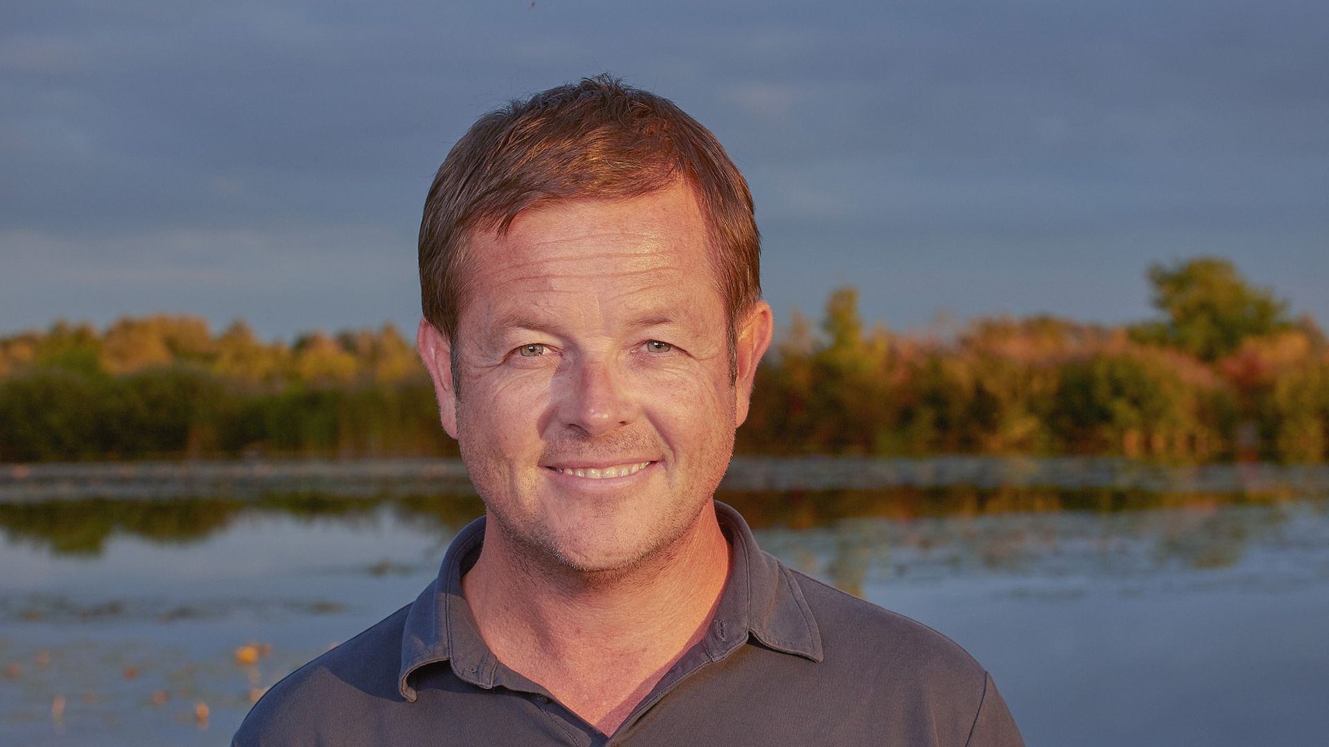 Andrew Morten, oprichter van TravelEssence, glimlachend buiten bij een meer