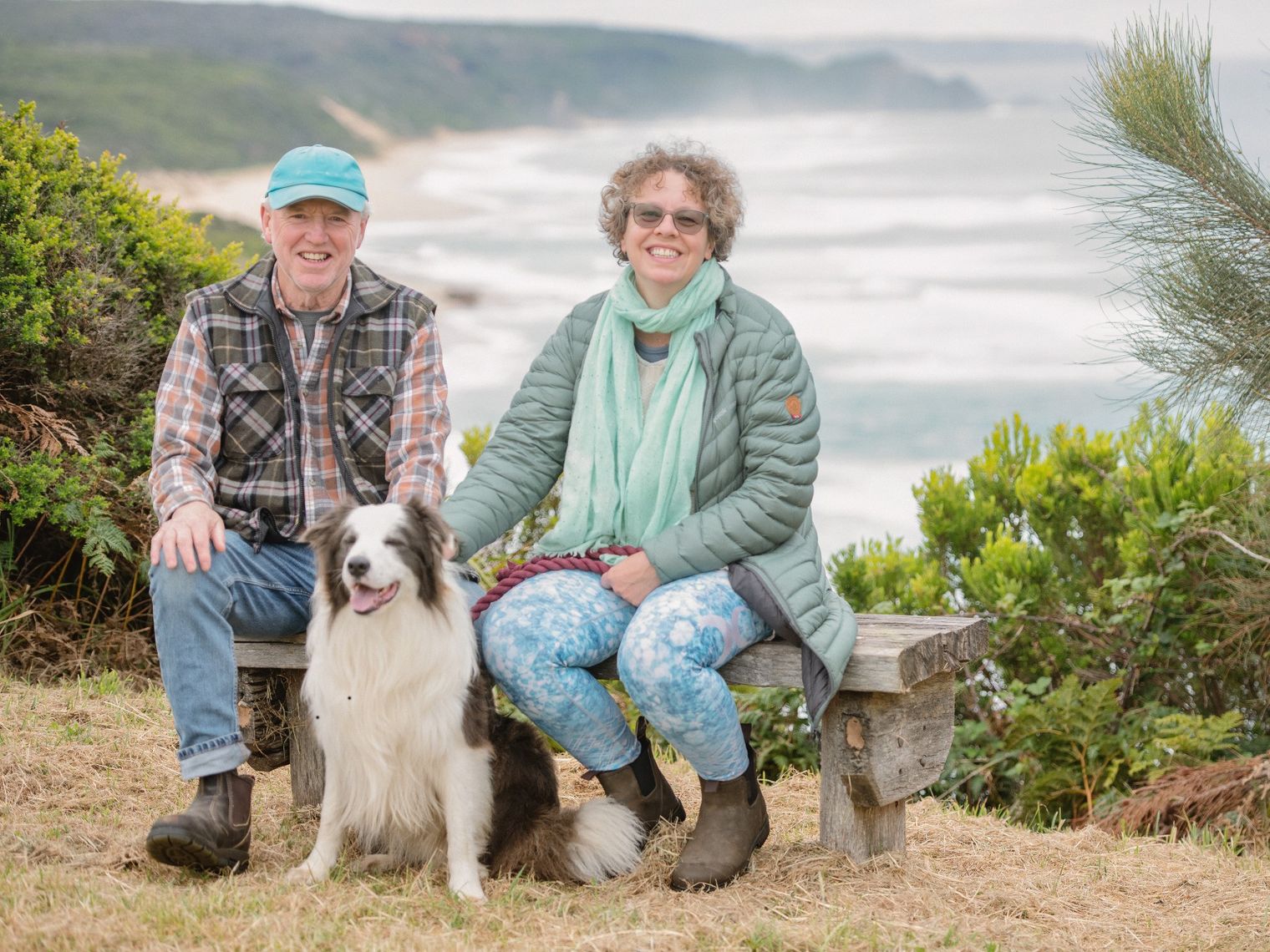 Couple sitting on a bench with their dog, overlooking a misty coastline