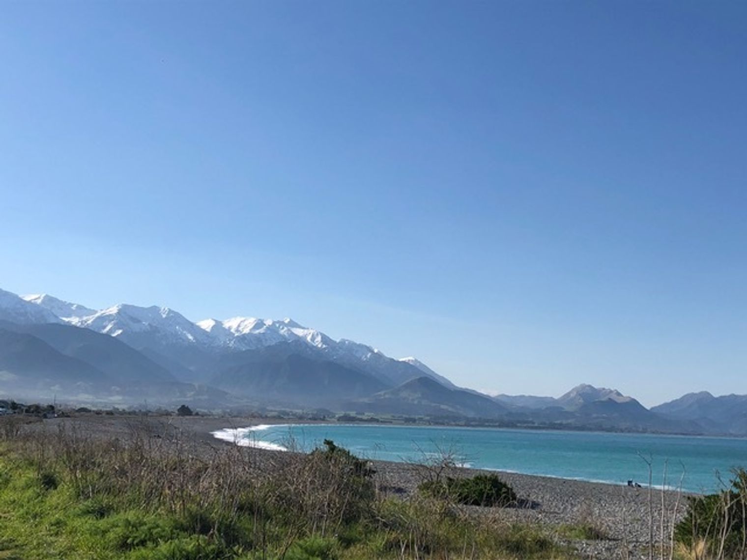 Blick auf den Ozean an der Küste mit schneebedeckten Bergen im Hintergrund in Kaikoura, Neuseeland