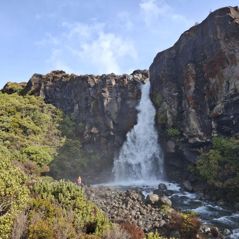 Wandelaar staat onder de Taranaki Falls die over een vulkanische rotswand storten in Tongariro National Park, Nieuw-Zeeland