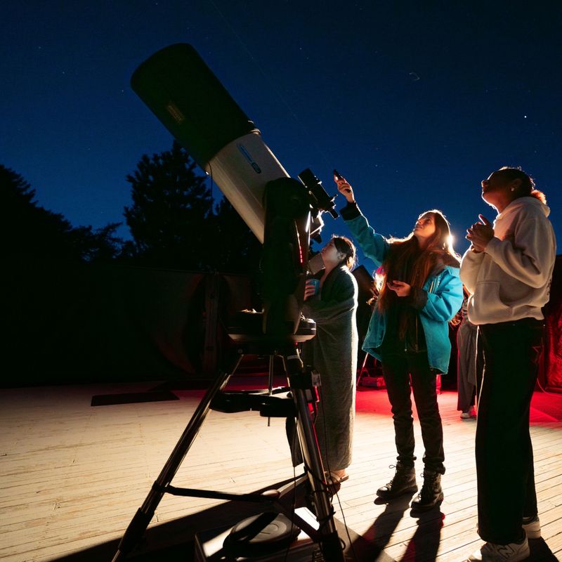 Bezoekers doen aan sterrenkijken met telescopen onder een sterrenhemel