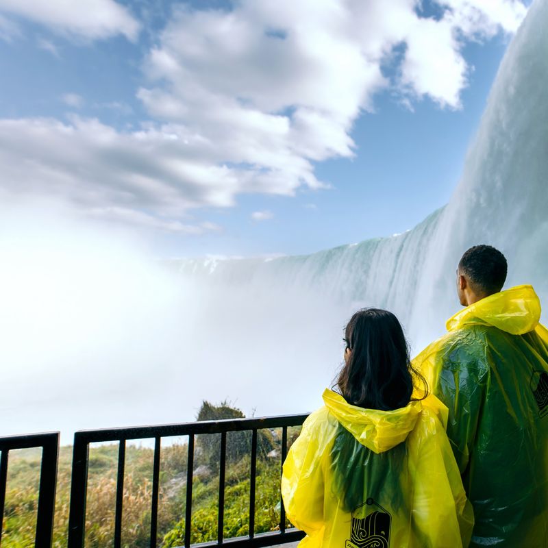 A couple wearing waterproof ponchos look up at the thundering Niagara Falls in Canada