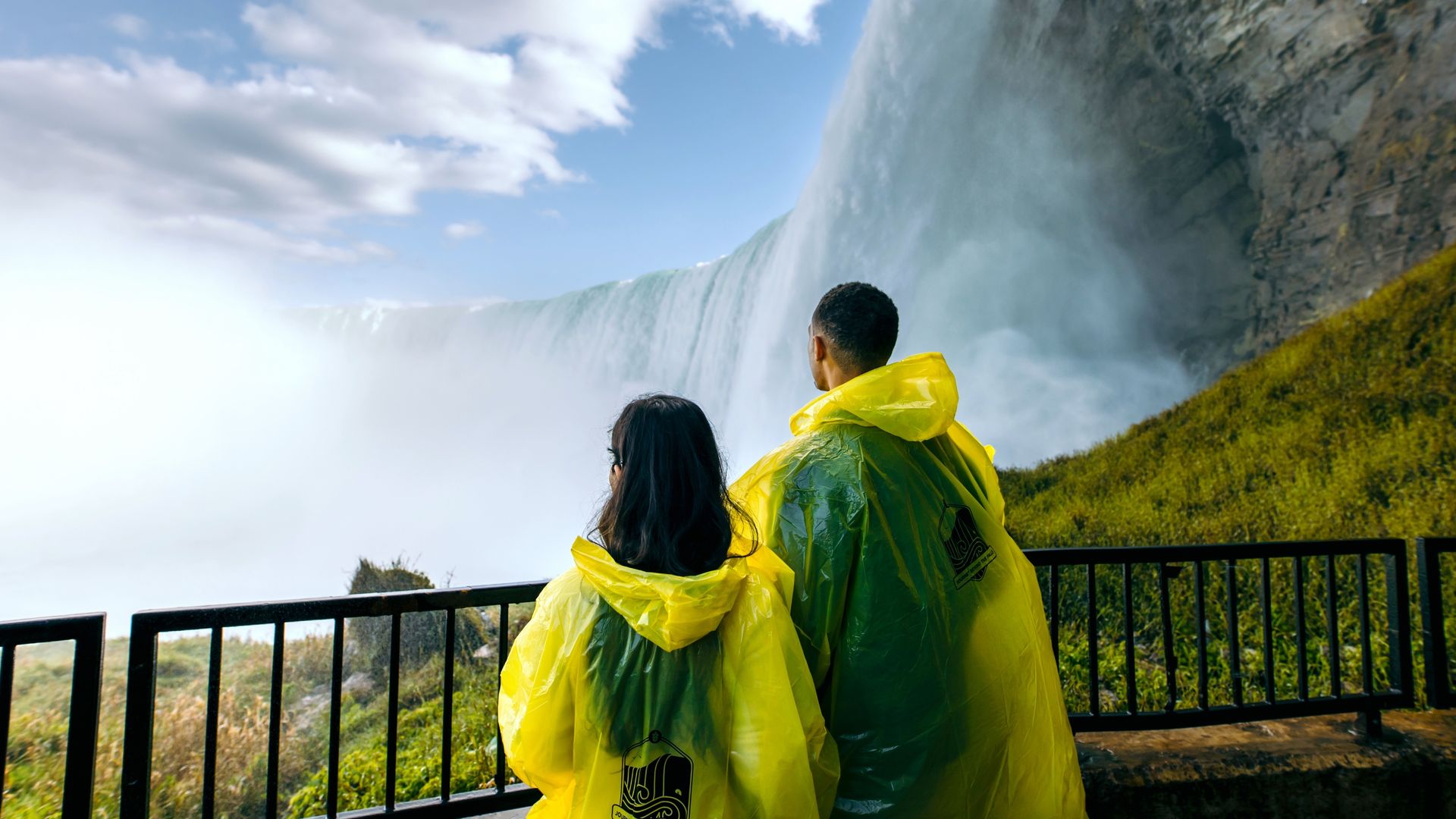 A couple wearing waterproof ponchos look up at the thundering Niagara Falls in Canada