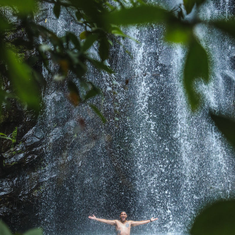 Een man staat met zijn armen wijd onder de Ellinjaa-waterval bij Atherton