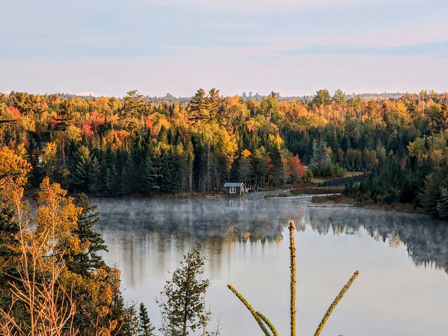 Am Ufer eines Sees, umgeben von einem farbenprächtigen Herbstwald, steht eine kleine Hütte