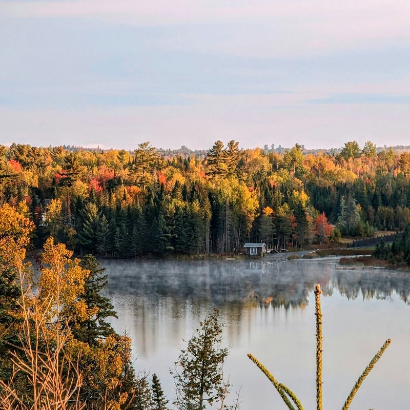 A small lodge sits on the edge of a lake surrounded by a colourful autumn forest