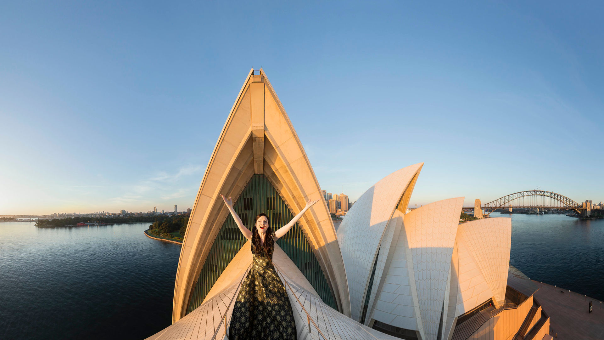 Künstlerin in Kostüm auf den Segeln des Sydney Opera House, im Hintergrund die Harbour Bridge