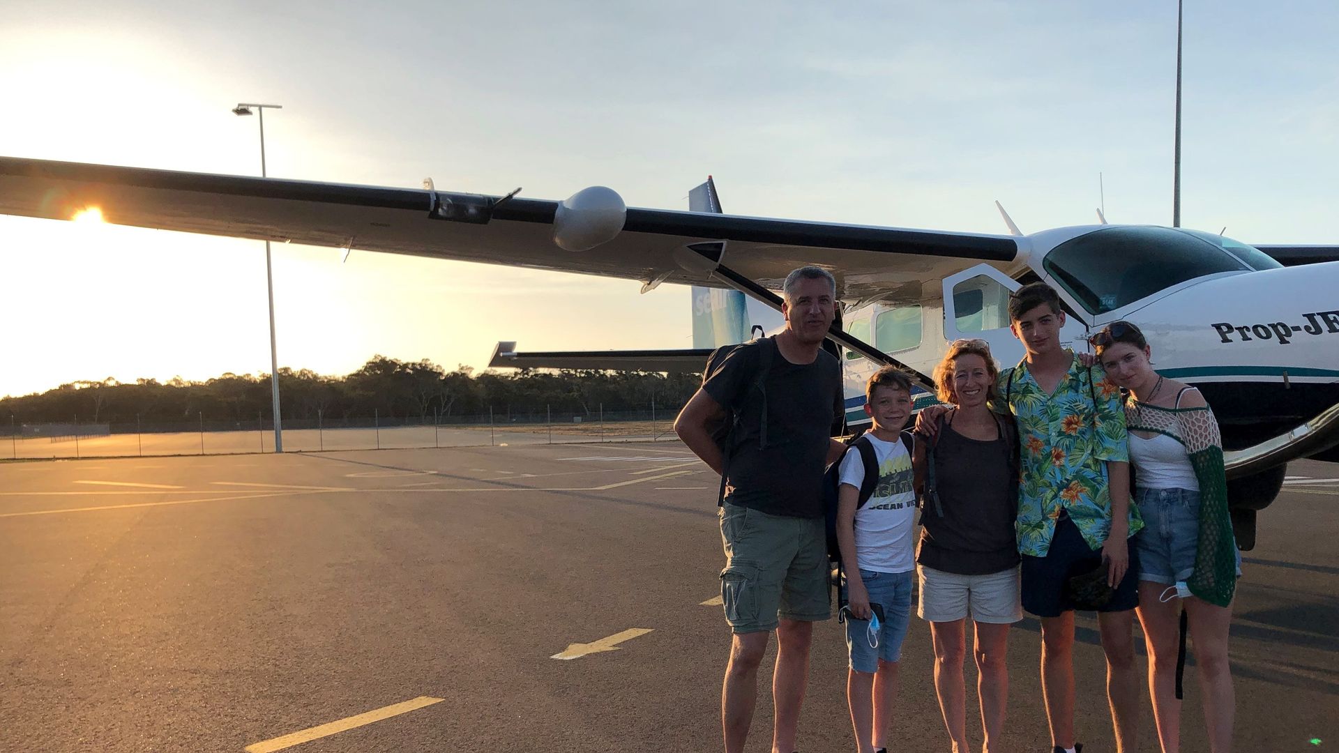 Familie steht auf dem Rollfeld neben einem kleinen Propellerflugzeug bei Sonnenuntergang in Australien