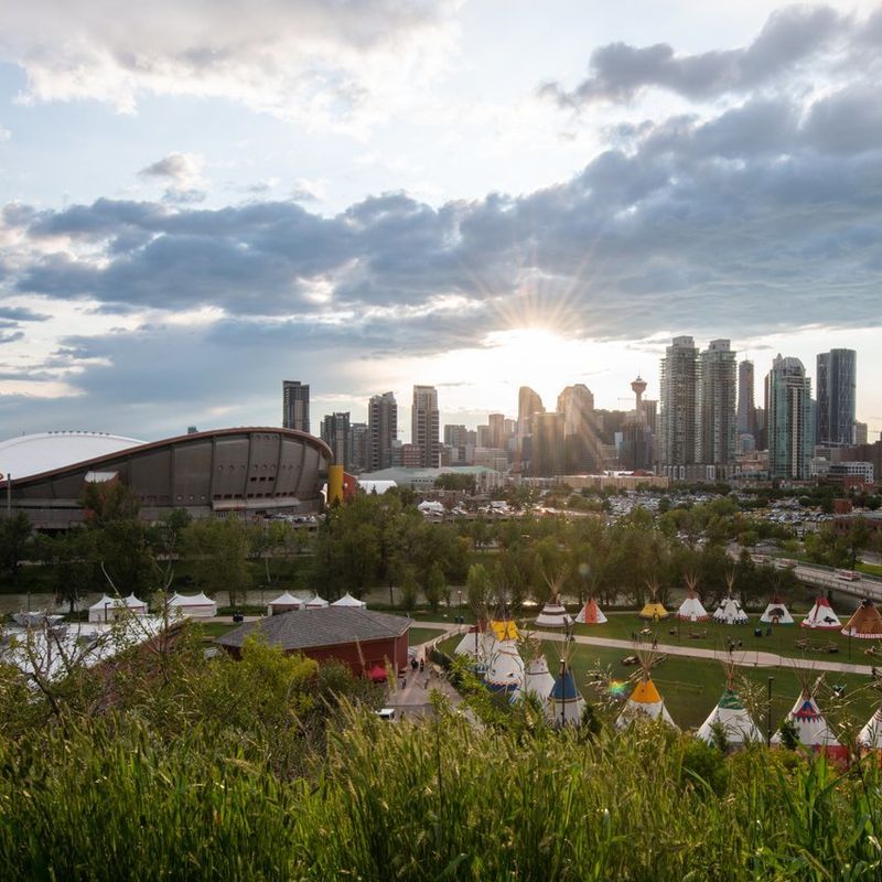 Stadsbeeld van de hoge gebouwen van Calgary met op de voorgrond een stadion en tipi's van de Calgary Stampede
