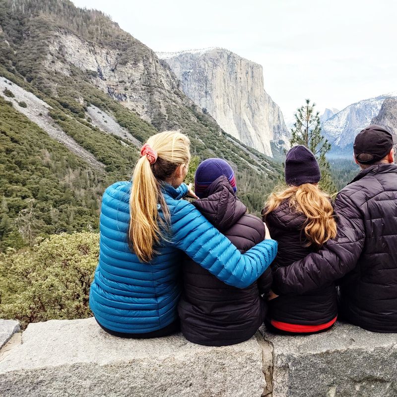 Eine vierköpfige Familie sitzt gemeinsam auf einer Mauer im Yosemite-Nationalpark und genießt den Blick auf hoch aufragende Granitfelsen und Wasserfälle