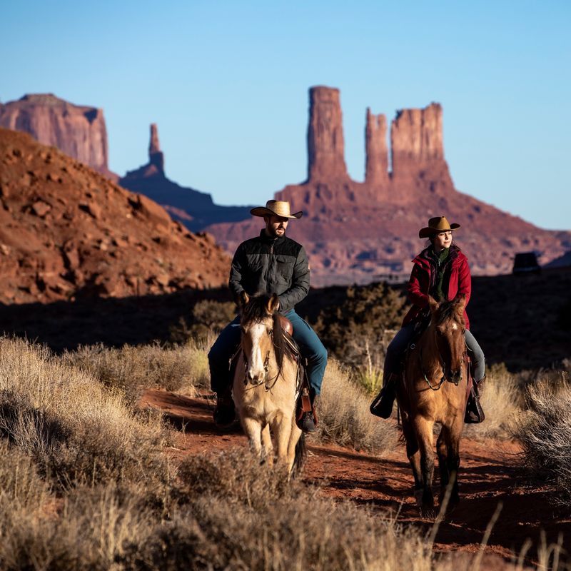 Twee mensen rijden op een paard door Monument Valley