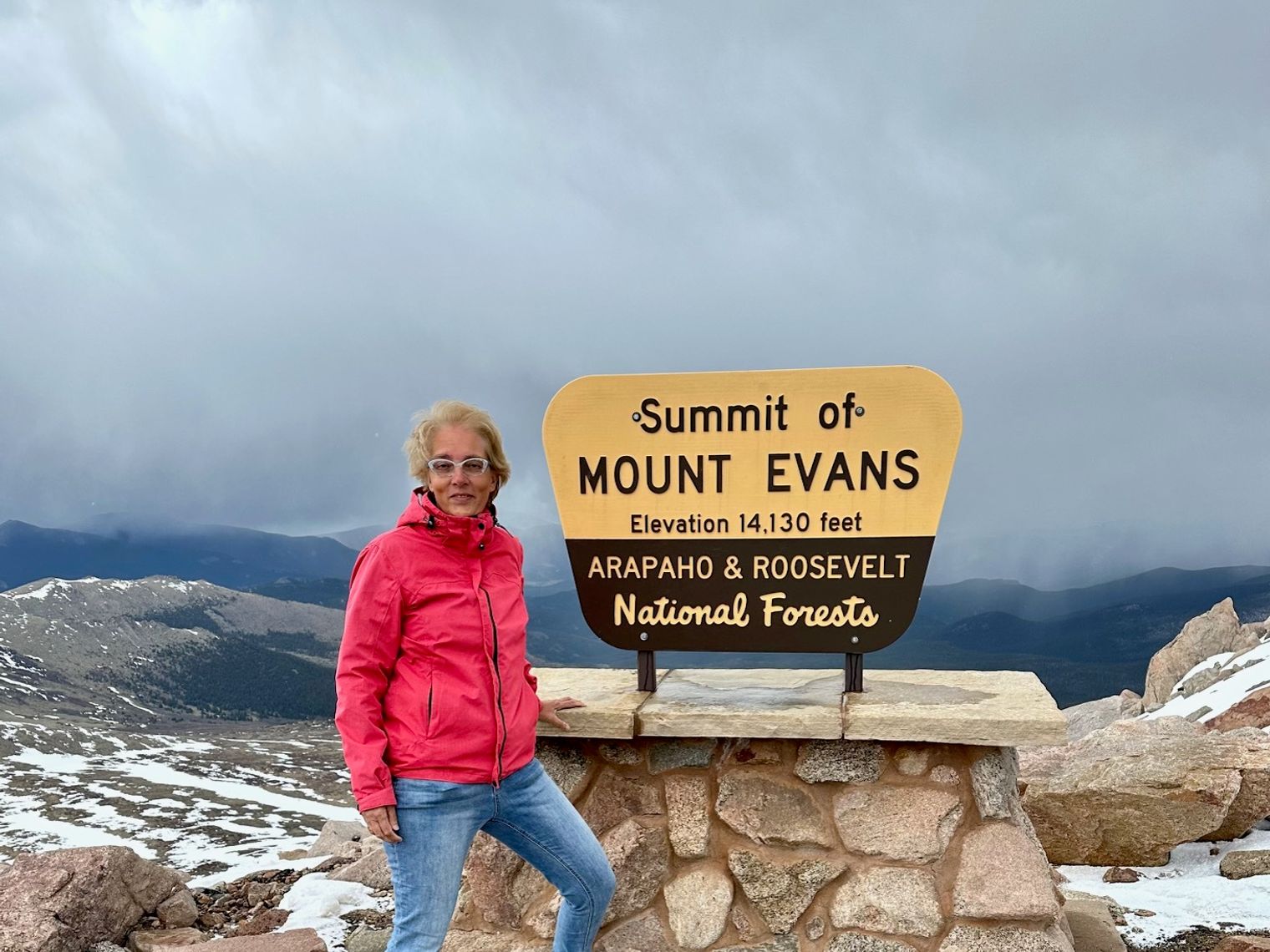 Mevrouw Cesar staat bij het summit bord op de top van Mount Evans
