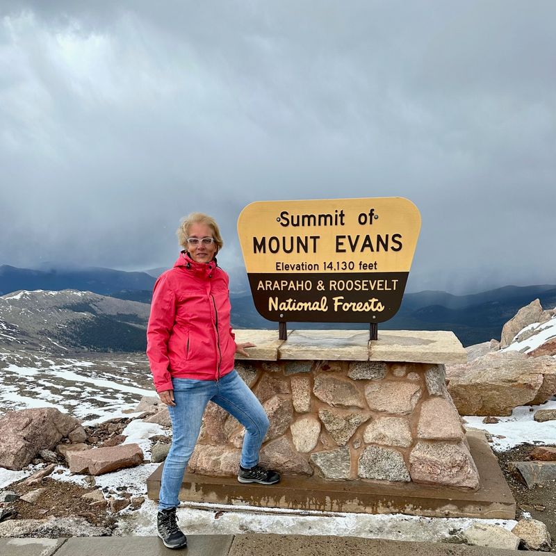 Mevrouw Cesar staat bij het summit bord op de top van Mount Evans