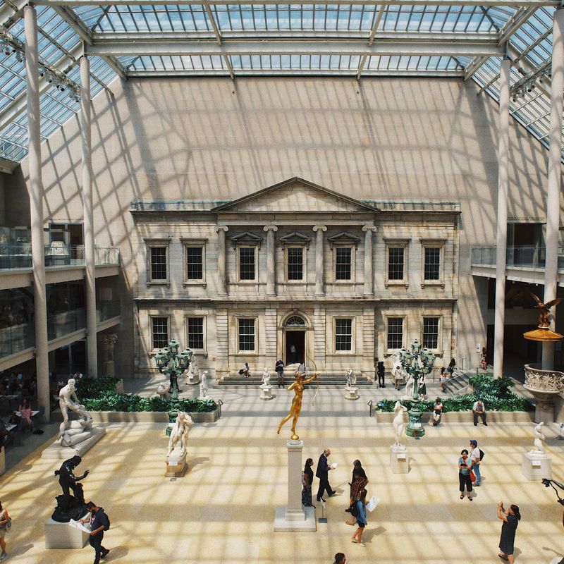 Bezoekers die door het Metropolitan Museum of Art in New York lopen, met standbeelden en een gevel