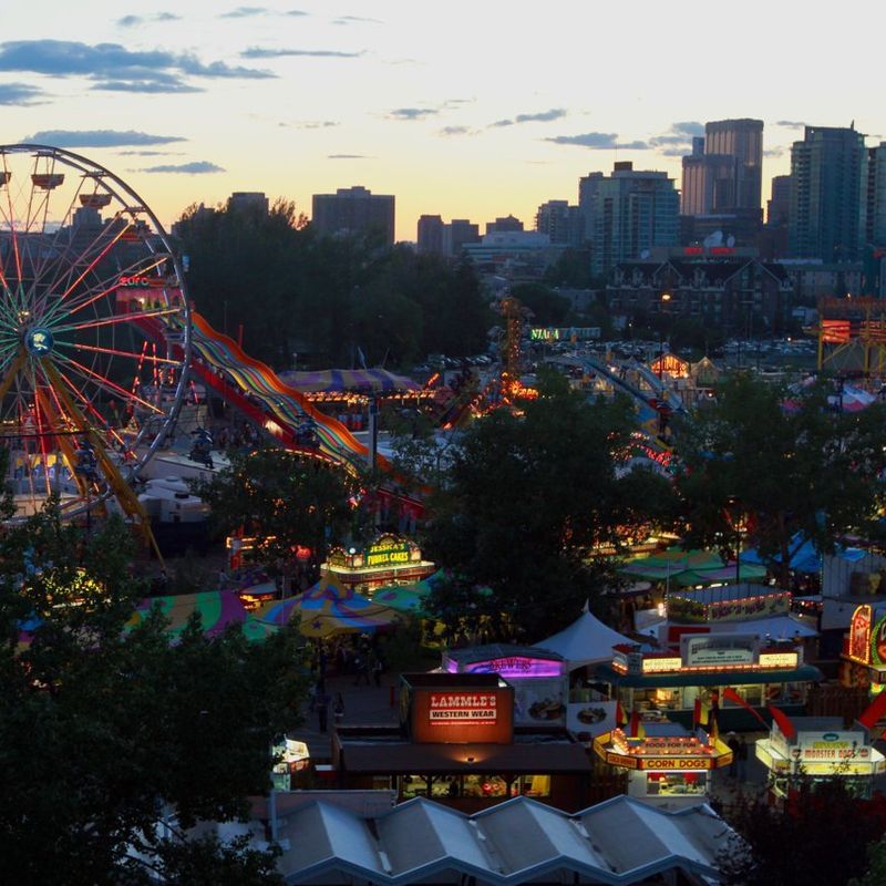 Calgary Stampede met een groot reuzenrad, een kleurrijke glijbaan en hoge gebouwen van de stad op de achtergrond
