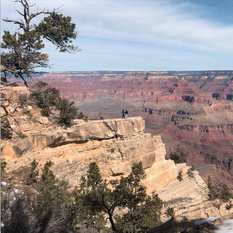Twee mensen staan aan de rand van een krater en kijken uit over de Grand Canyon in Arizona.