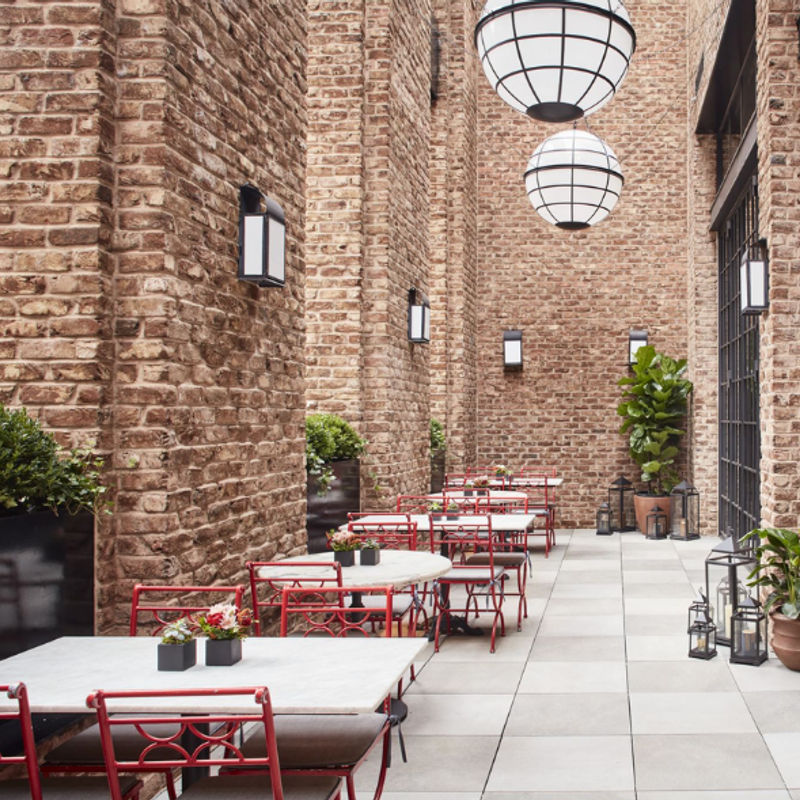 Een restaurantje in een historisch hotel in New York, rode stoelen en witte tafels tussen stenen muren
