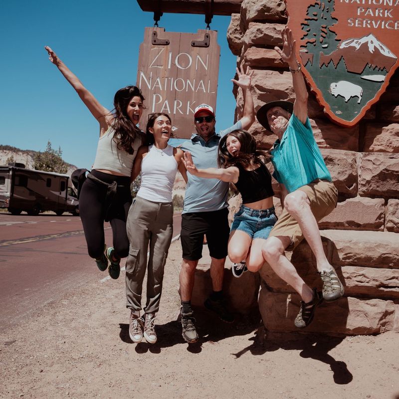 Een groep vrolijke mensen springt bij het entreebord van Zion National Park