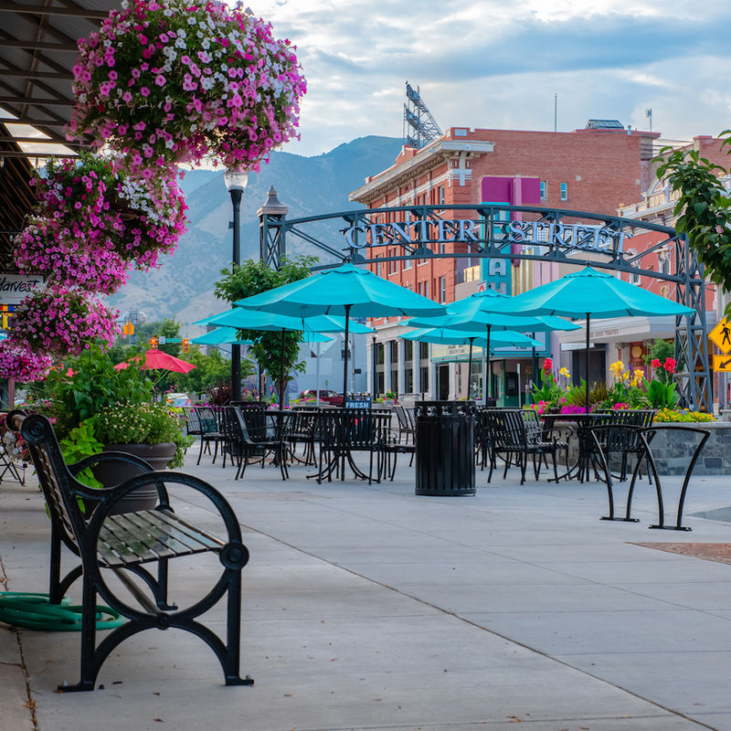 Friedliche Einkaufsstraße mit Blumen und blauen Schirmen in Logan